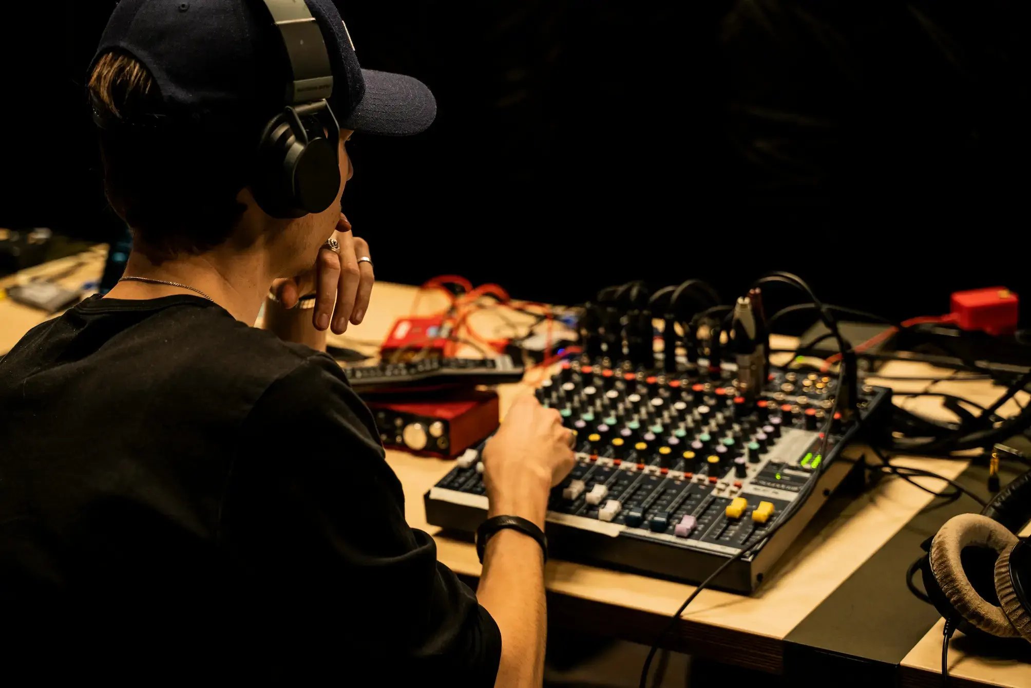person wearing headphones adjusting knobs on a compact audio mixing console with colorful dials and sliders