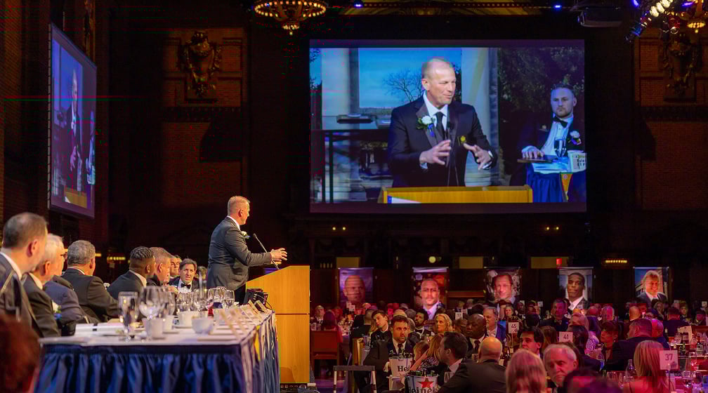 man presenting on stage to a crowd on i-mag screen